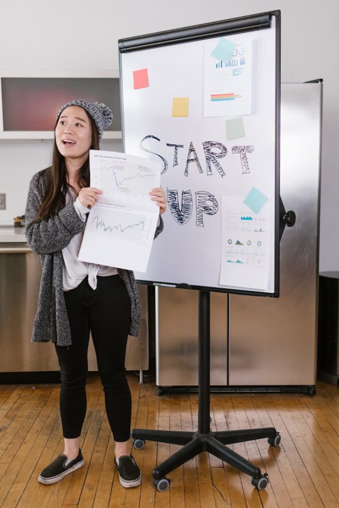 A young woman gives a startup presentation with charts and graphs on a flipchart.